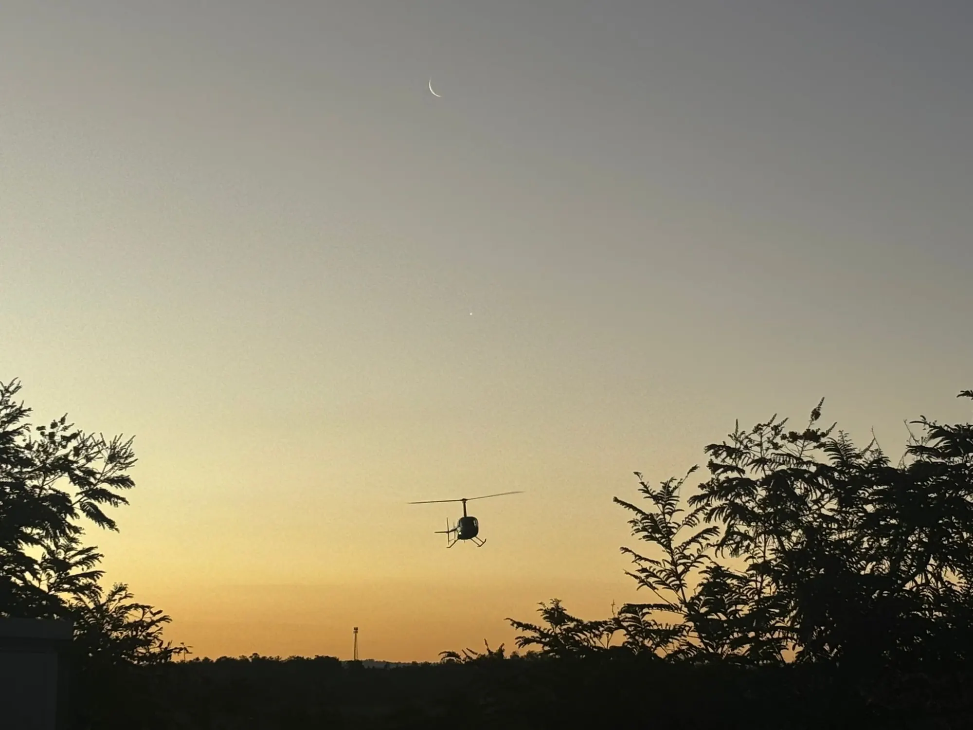 Distant helicopter silhouette under a crescent moon